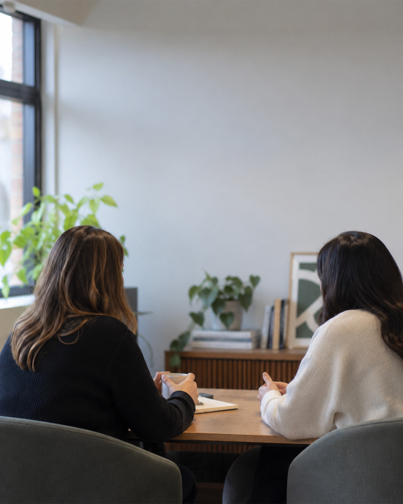 Two people talking across a wooden table in a quiet, naturally lit meeting room.